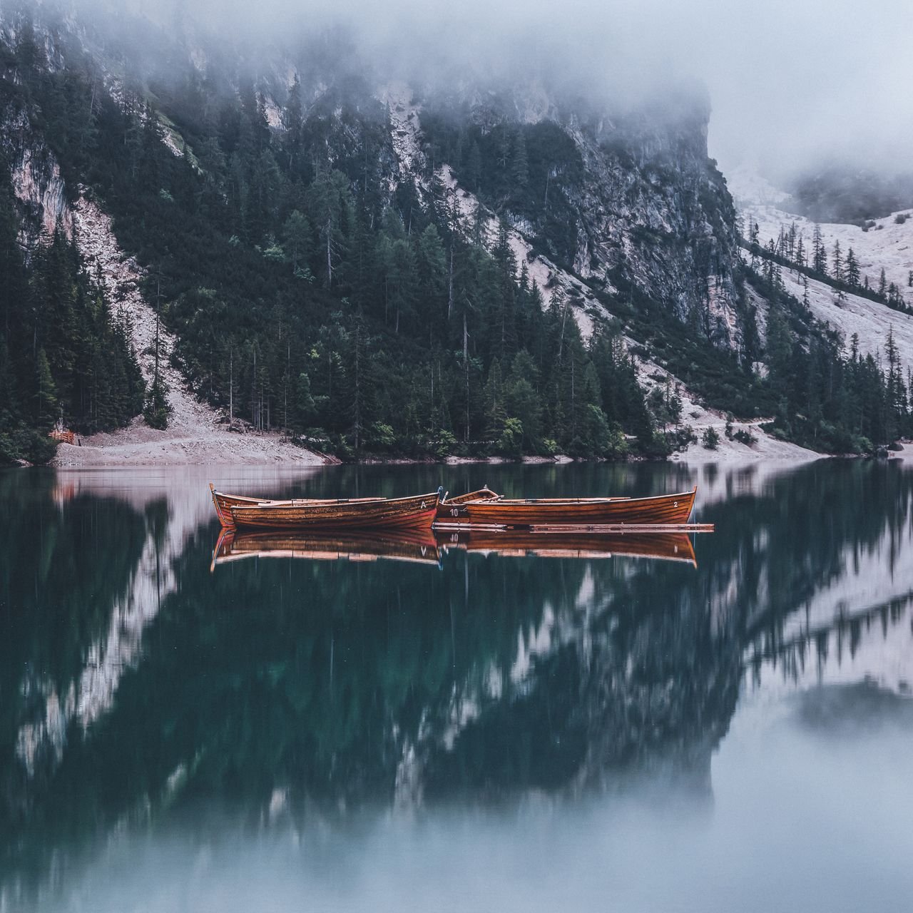 Two wooden rowboats resting on a still, misty mountain lake